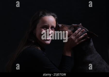 Porträt einer lachenden Frau und eines Doberman-Hundes, der ihr Gesicht mit seiner Schnauze berührt, Studiofoto Stockfoto