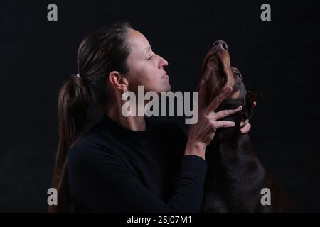 Junge Frau mit Doberman-Hund mit erhobenem Kopf, auf schwarzem Hintergrund Stockfoto