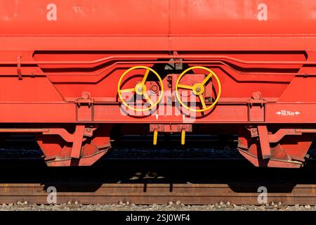 Leuchtend gelbe Handbremsen sind an einem roten Güterzugwagen sichtbar. Die robuste Metallkonstruktion steht vor einem Hintergrund aus Kies in einem Stockfoto