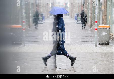 Hannover, Deutschland. Februar 2025. Eine Frau mit einem Regenschirm wird während des Schneefalls in der Glasscheibe eines Vitrinenregals reflektiert. Quelle: Julian Stratenschulte/dpa/Alamy Live News Stockfoto