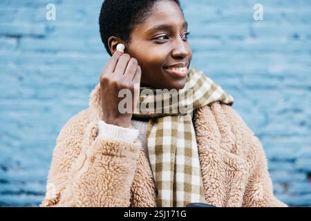 Junge Frau, die Ohrstöpsel trägt und lächelt, während sie im Winter draußen steht Stockfoto