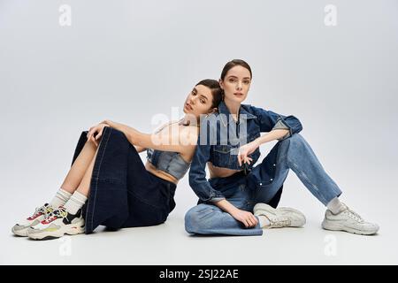 Zwei schöne Schwestern sitzen bequem auf dem Boden und strahlen Vertrauen und Stil aus. Stockfoto