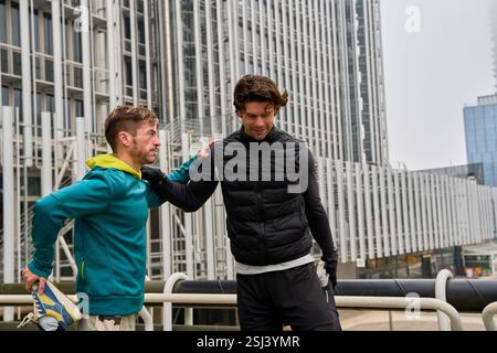 Zwei männliche Athleten, die ihre Beine nach dem Training im Freien in einer modernen urbanen Umgebung Strecken Stockfoto