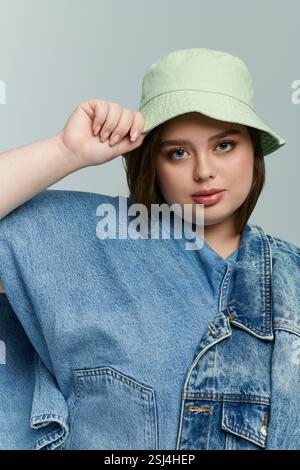 Die junge Frau in Übergröße zeigt ihren einzigartigen Sinn für Mode mit Denim-Lagen und einem schicken Hut. Stockfoto