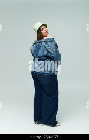 Die junge Frau zeigt einen trendigen Denim-Stil in Übergröße, während sie drinnen Selbstvertrauen und Charme ausstrahlt. Stockfoto