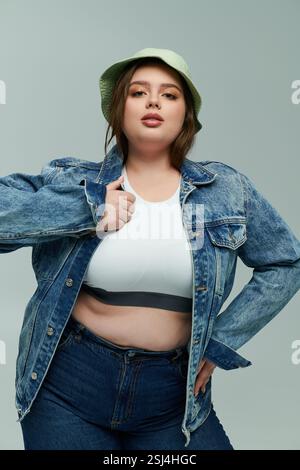 Eine junge Frau in Übergröße zeigt selbstbewusst ihren Sinn für Mode in einer Jeansjacke und -Mütze. Stockfoto