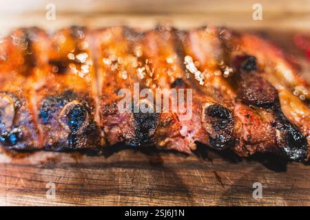 Blick von oben auf köstliche gegrillte Schweinerippchen mit Ketchup und Senf, serviert auf einem Holzbrett. Ein Gericht zum Bier in einem Fleischrestaurant. Ausgewählter Fokus. Hochwertige Fotos Stockfoto