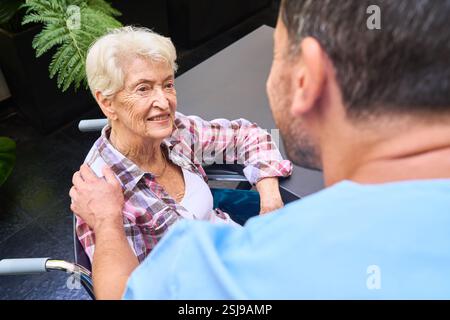 Freundliche Interaktion in einer Seniorenpflegeeinrichtung mit einer Pflegeperson, die eine ältere Frau unterstützt. Stockfoto