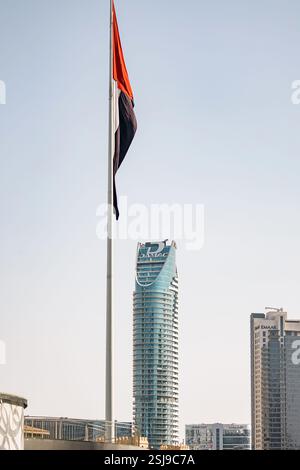 Flagge der Vereinigten Arabischen Emirate und Glashochhaus mit Logo des Damac Entwicklungsunternehmens. Hohes Gebäude, Stadtbild. DAMAC Maison Distinction Hotel zu Stockfoto
