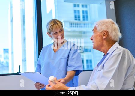 Eine Krankenschwester in blauer Uniform mit einem älteren männlichen Patienten in einer Pflegeeinrichtung. Die Szene zeigt ein professionelles Gesundheitsumfeld mit Fokus auf Stockfoto
