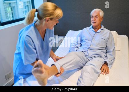 Eine Pflegekraft, die einem älteren Mann in einer Rehabilitationseinrichtung hilft, wobei der Schwerpunkt auf Mobilität liegt. Der Profi bietet Therapie, präsentiert Seniorenbetreuung und Stockfoto