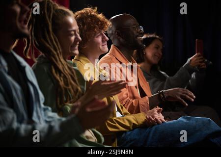 Eine Gruppe von verschiedenen Personen saß in einem Theater und genoss und applaudierte eine Vorstellung auf der Bühne. Ihre fröhlichen Ausdrücke zeigen die Wertschätzung und Begeisterung für die Handlung Stockfoto
