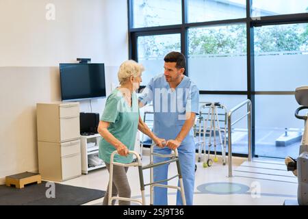 Eine Physiotherapeutin hilft einer älteren Frau mit einem Gehhilfen in einer Rehabilitationseinrichtung und konzentriert sich dabei auf Balance- und Bewegungstraining, um ihre Arbeit zu verbessern Stockfoto