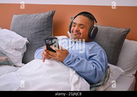 Mann mit Down-Syndrom, der Musik im Bett hört Stockfoto