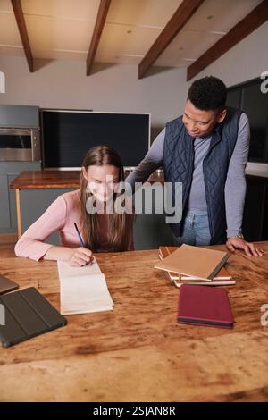 Mann Assisting Girl (12-13) schreibt in Notizblock Stockfoto