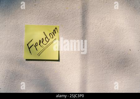 Eine gelbe Haftnotiz mit „Freiheit“ in Fettschrift, platziert auf einer dunklen strukturierten Oberfläche, die Stärke, Wahl und Befreiung repräsentiert. Stockfoto