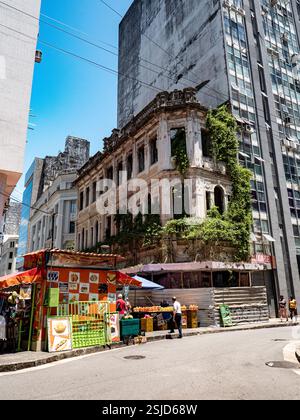Salvador de Bahia, Brasilien. Blick auf die Straße mit einem alten verlassenen Gebäude, das von der Natur übernommen wurde, neben dem neuen Wolkenkratzer Stockfoto