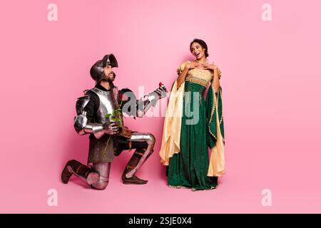 Liebhaber des Mittelalters in Theaterkostümen posieren liebevoll vor einem leuchtend rosa Hintergrund und verkörpern Romantik und Eleganz Stockfoto