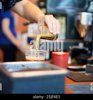 Der Barista gießt Espresso in Eiskaffee an einem geschäftigen Café in Kalifornien, USA, und zeigt Details zur Getränkezubereitung und zum Service, August 2024 Stockfoto