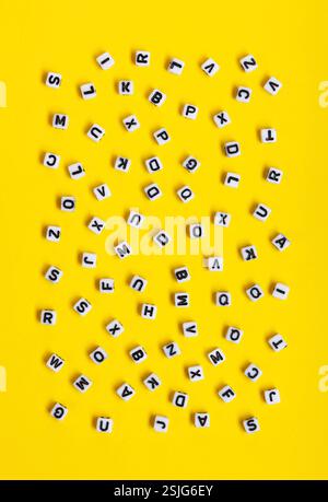 Weiße Würfel mit zufällig verstreuten Buchstaben auf gelbem Hintergrund. Das Bild kann für viele Zwecke, Bucheinbände oder Konzepte im Zusammenhang mit Grammatik und Typografie verwendet werden. Stockfoto