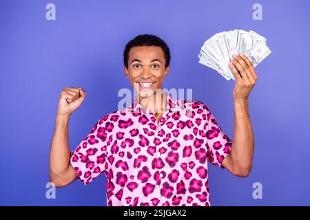 Lächelnder Mann, der Erfolg feiert und Bargeld vor leuchtendem lila Hintergrund hält Stockfoto