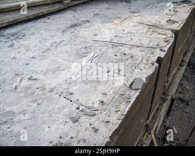 Nahaufnahme von gerissenen, verwitterten Betonplatten mit freiliegendem Bewehrungsstahl, die Alterungs- und strukturelle Probleme im Baumaterial aufzeigen. Stockfoto