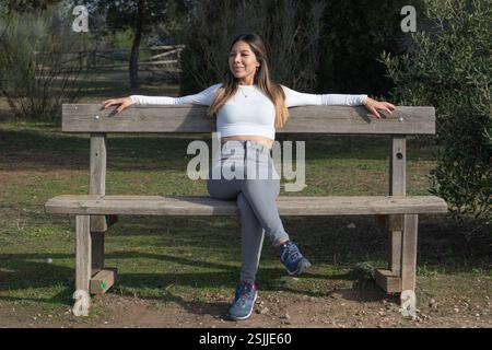 Eine junge Frau, die auf einer Holzbank sitzt und die Sonne und die Natur genießt Stockfoto