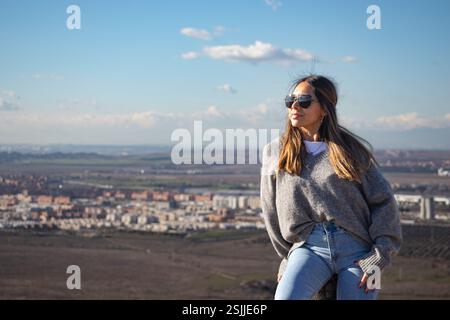 Eine junge Frau, die auf einem Hügel sitzt und eine Sonnenbrille trägt Stockfoto
