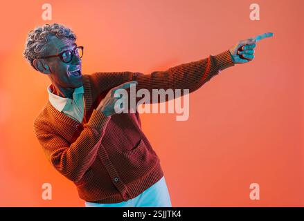 Senior-Mann posiert im Studio. Lustiger Seniorenmann mit durchschnittlichem Pullover, der auf farbigen Hintergründen posiert. Studio-Aufnahme mit farbigen Gellichtern. Stockfoto