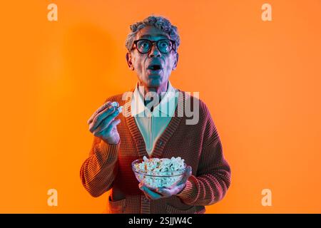 Senior-Mann posiert im Studio. Lustiger Seniorenmann mit durchschnittlichem Pullover, der auf farbigen Hintergründen posiert. Studio-Aufnahme mit farbigen Gellichtern. Stockfoto