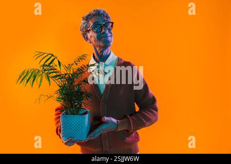 Senior-Mann posiert im Studio. Lustiger Seniorenmann mit durchschnittlichem Pullover, der auf farbigen Hintergründen posiert. Studio-Aufnahme mit farbigen Gellichtern. Stockfoto