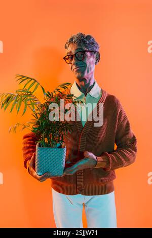 Senior-Mann posiert im Studio. Lustiger Seniorenmann mit durchschnittlichem Pullover, der auf farbigen Hintergründen posiert. Studio-Aufnahme mit farbigen Gellichtern. Stockfoto