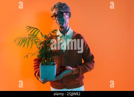 Senior-Mann posiert im Studio. Lustiger Seniorenmann mit durchschnittlichem Pullover, der auf farbigen Hintergründen posiert. Studio-Aufnahme mit farbigen Gellichtern. Stockfoto