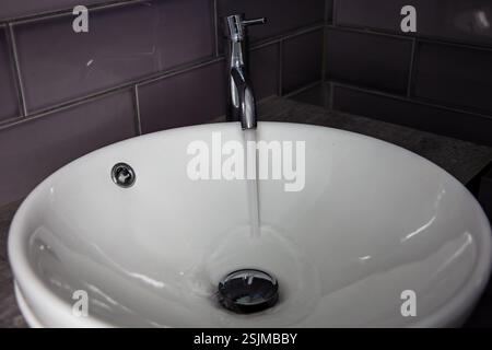 Kreisförmiges weißes Keramikwaschbecken mit Chromhahn, aus dem Wasser austritt Stockfoto