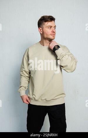 Ein modischer und trendiger Mann posiert selbstbewusst, während er ein stilvolles beiges Sweatshirt und eine elegante schwarze Hose trägt Stockfoto