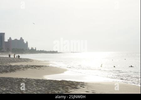 Strand bei Sonnenaufgang. Sanftes, trübes Licht überschwemmt die Szene und hebt die fernen Gebäude und das ruhige Meer hervor. Ruhe und Gelassenheit. Ein Moment der Ruhe Stockfoto
