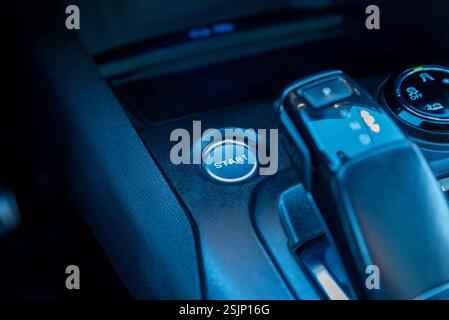 Nahaufnahme der Starttaste eines Fahrzeugs und der Mittelkonsole mit Gangschaltung, die den modernen Fahrzeuginnenraum, die intelligenten Bedienelemente und die Druckknopfausrichtung veranschaulicht Stockfoto