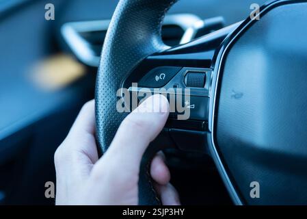 Nahaufnahme einer Hand, die die Sprachbefehlstaste am Lenkrad drückt, zeigt Smart-Car-Technologie, KI-gesteuerte Assistenz und freihändiges Fahren Stockfoto