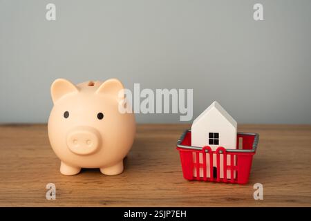 Schweinebank mit Haus im Einkaufswagen. Konzept des Kaufs, Verkaufs oder Mietens einer Wohnung. Hypotheken, Kredite, Immobilien Stockfoto