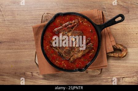 Gebratenes Steak, Kalbshals auf dem Knochen, gedünstet mit Gemüse, in Tomatensauce, Fleisch kochen, in einer gusseisernen Pfanne, Draufsicht, keine Leute Stockfoto
