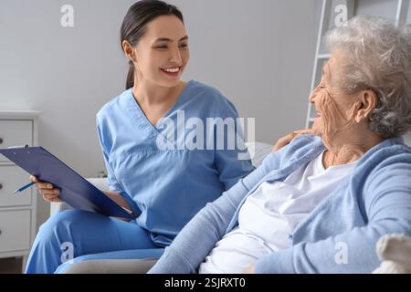 Physiotherapeutin mit Klemmbrett und ältere Frau, die zu Hause auf dem Sofa sitzt Stockfoto