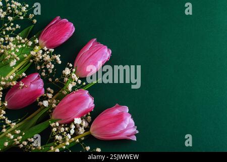 Pinkfarbene Tulpen mit Babyblüten auf tiefgrünem Hintergrund für einen satten Kontrast und ein elegantes Blumenarrangement. Draufsicht, Kopierraum. Stockfoto