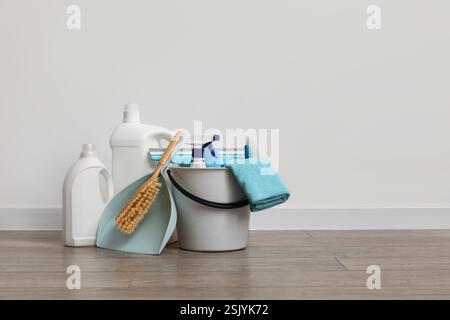 Eimer mit Reinigungsprodukten und Kehrschaufel auf Laminatboden gegen weiße Wand Stockfoto
