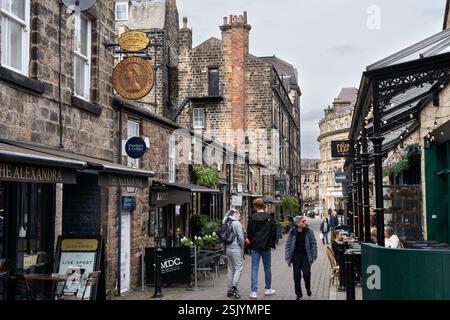Menschen gehen an traditionellen Sandsteingebäuden vorbei, Cafés, Bars und Restaurants in der John Street in der Altstadt von Harrogate, England Stockfoto