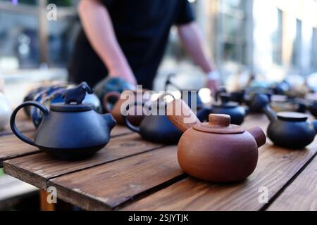 Teekanne aus Ton und handgemachte Gerichte auf Holztisch. Traditionen der ukrainischen Töpferei. Ein Mann in schwarzer Schürze steht neben Tongeschirr. Tee-Set für die Küche. Stockfoto