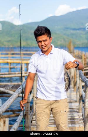 Ein junger philippinischer Mann in einem weißen Hemd zeigt einen frisch gefangenen Tilapia auf einer Fischfarm in Lake Buhi, Bicol, Philippinen Stockfoto