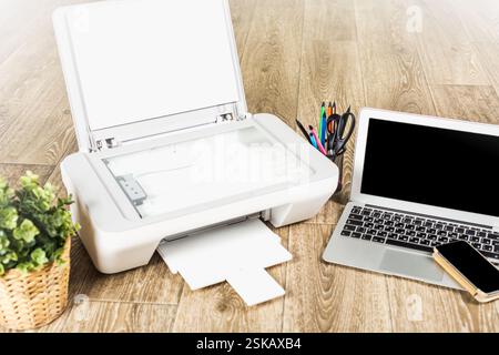 Das Home Office verfügt über einen Drucker, Laptop und Schreibwaren mit einer Innenanlage auf Holzboden zur Steigerung der Produktivität Stockfoto
