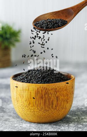 Schwarze Sesamsamen fallen vom Löffel in die Schüssel auf den Tisch Stockfoto