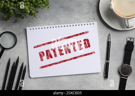 Lizenz. Notizbuch mit patentiertem rotem Stempel, Schreibwaren und Armbanduhr auf grauem Tisch, Draufsicht Stockfoto