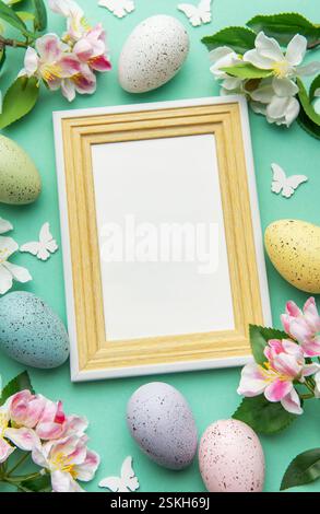 Ostereier, Frühlingsblumen, Schmetterlinge und ein leerer Rahmen schaffen eine festliche Grenze auf türkisfarbenem Hintergrund Stockfoto